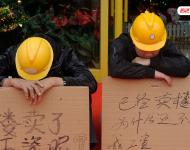 2012年12月25日，廣東中山，火炬開發區的多名建筑工人討要工作一年多的血汗錢一籌莫展，一些工人干脆將鋪蓋卷搬到了售樓部，并在門口搭起灶臺煮飯，希望以這種方式討回工錢。圖為在銷售中心門外，工人舉牌討薪。吳進/視覺中國